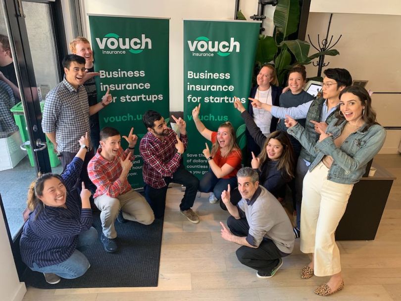 A group of employees at Vouch pose together in front of company banners.