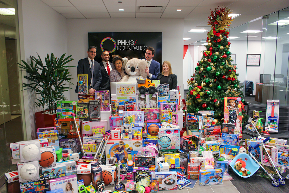 Five PHMG staff pictured in front of an absurdly large pile of toys